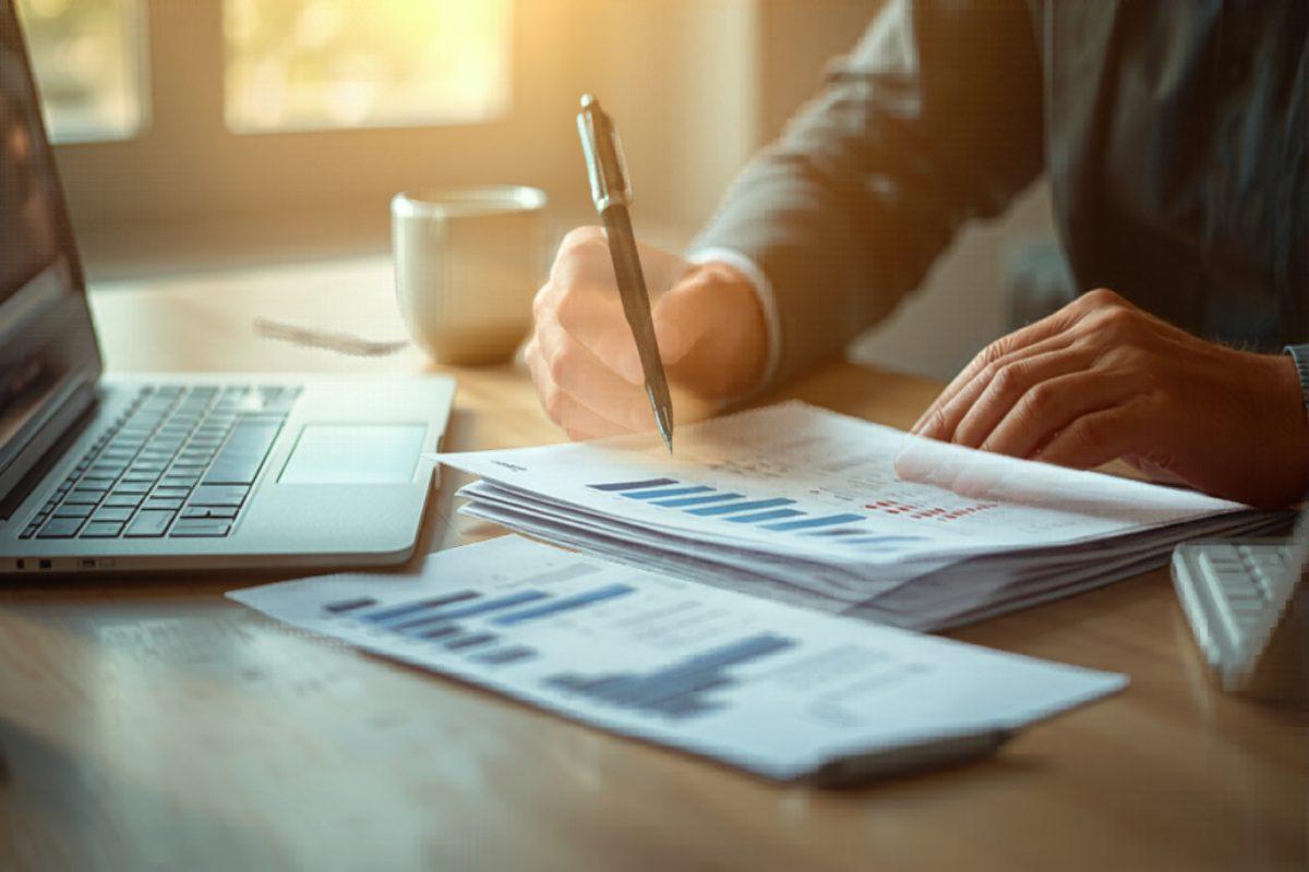 Small business owner reviewing invoices at a wooden desk with a laptop and coffee, warm afternoon light